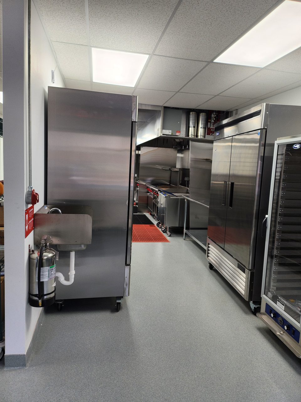 Hand-washing sink next to tall stainless steel commercial fridges